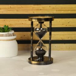 An antique brass hourglass with black sand and bamboo-style pillars, featuring a vintage compass design on the base.