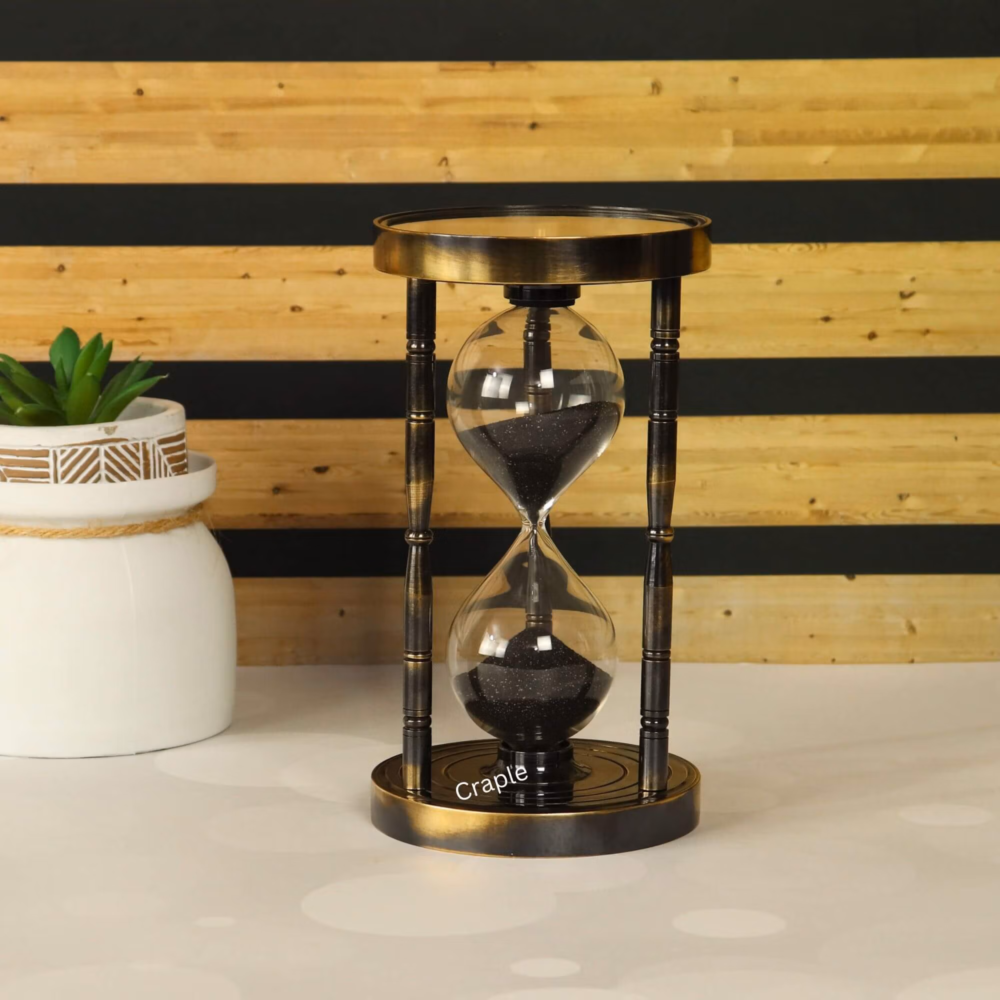 Top & Bottom Compass Brass Hourglass Black Antique Finish-1 An antique brass hourglass with black sand and bamboo-style pillars, featuring a vintage compass design on the base.
