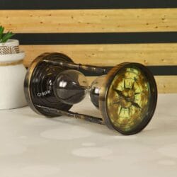 The antique brass sand timer resting horizontally, showing the vintage compass face on one end.