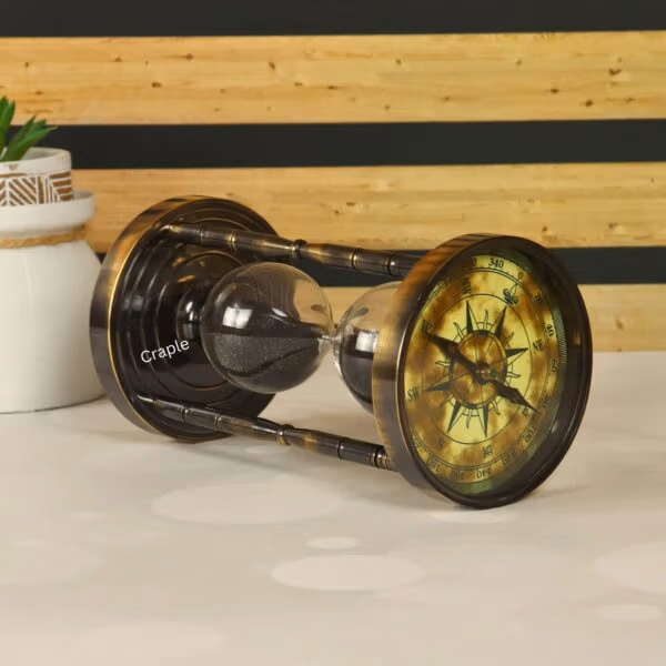 The antique brass sand timer resting horizontally, showing the vintage compass face on one end.