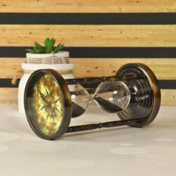 Angled view of the black sand hourglass lying on its side, highlighting the antique brass finish and compass dial.