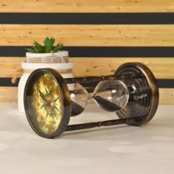 Angled view of the black sand hourglass lying on its side, highlighting the antique brass finish and compass dial.