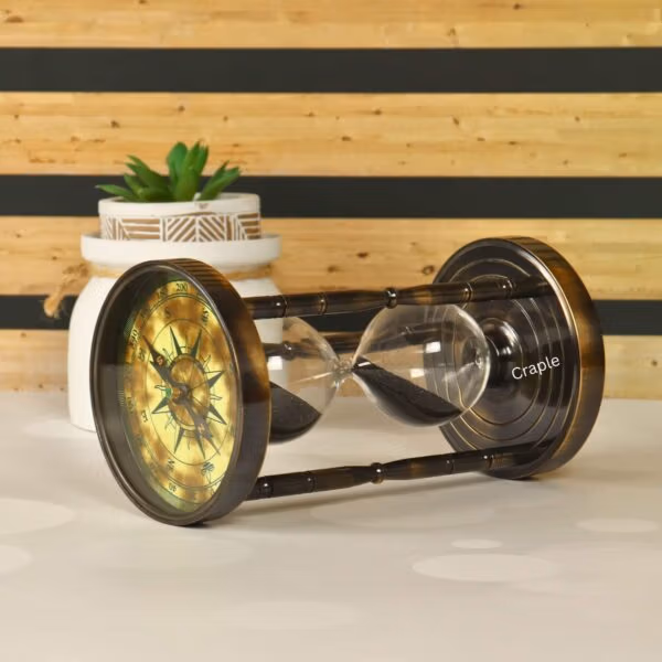 Angled view of the black sand hourglass lying on its side, highlighting the antique brass finish and compass dial.