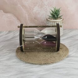 The triple sand timer resting horizontally on a decorative mat, showing the three different colored sand hourglasses.