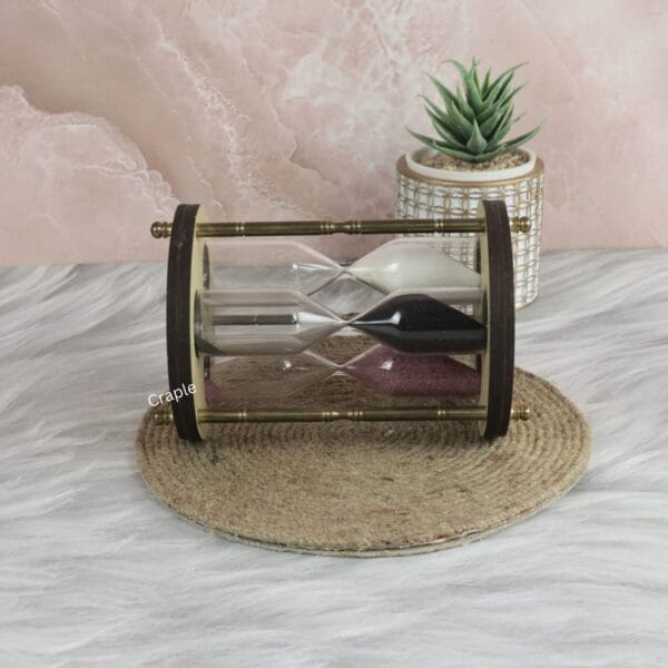 The triple sand timer resting horizontally on a decorative mat, showing the three different colored sand hourglasses.