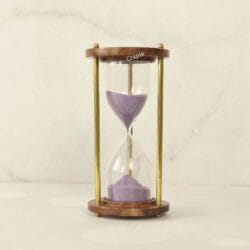 A vintage 5-minute hourglass with purple sand, framed by round wooden bases and elegant brass pillars.