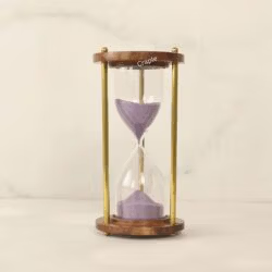 A vintage 5-minute hourglass with purple sand, framed by round wooden bases and elegant brass pillars.