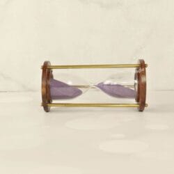 The wooden and brass sand timer resting horizontally, showcasing its classic construction and purple sand.