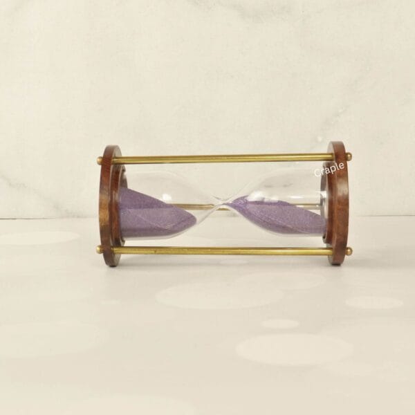 The wooden and brass sand timer resting horizontally, showcasing its classic construction and purple sand.