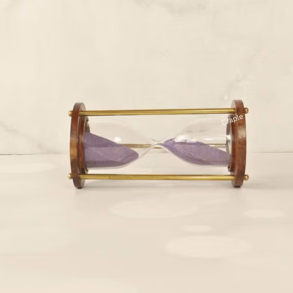 The wooden and brass sand timer resting horizontally, showcasing its classic construction and purple sand.