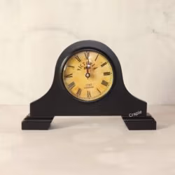 Vintage Victoria-style mantel clock with a black antique finish, a round aged-yellow dial, and classic Roman numerals.