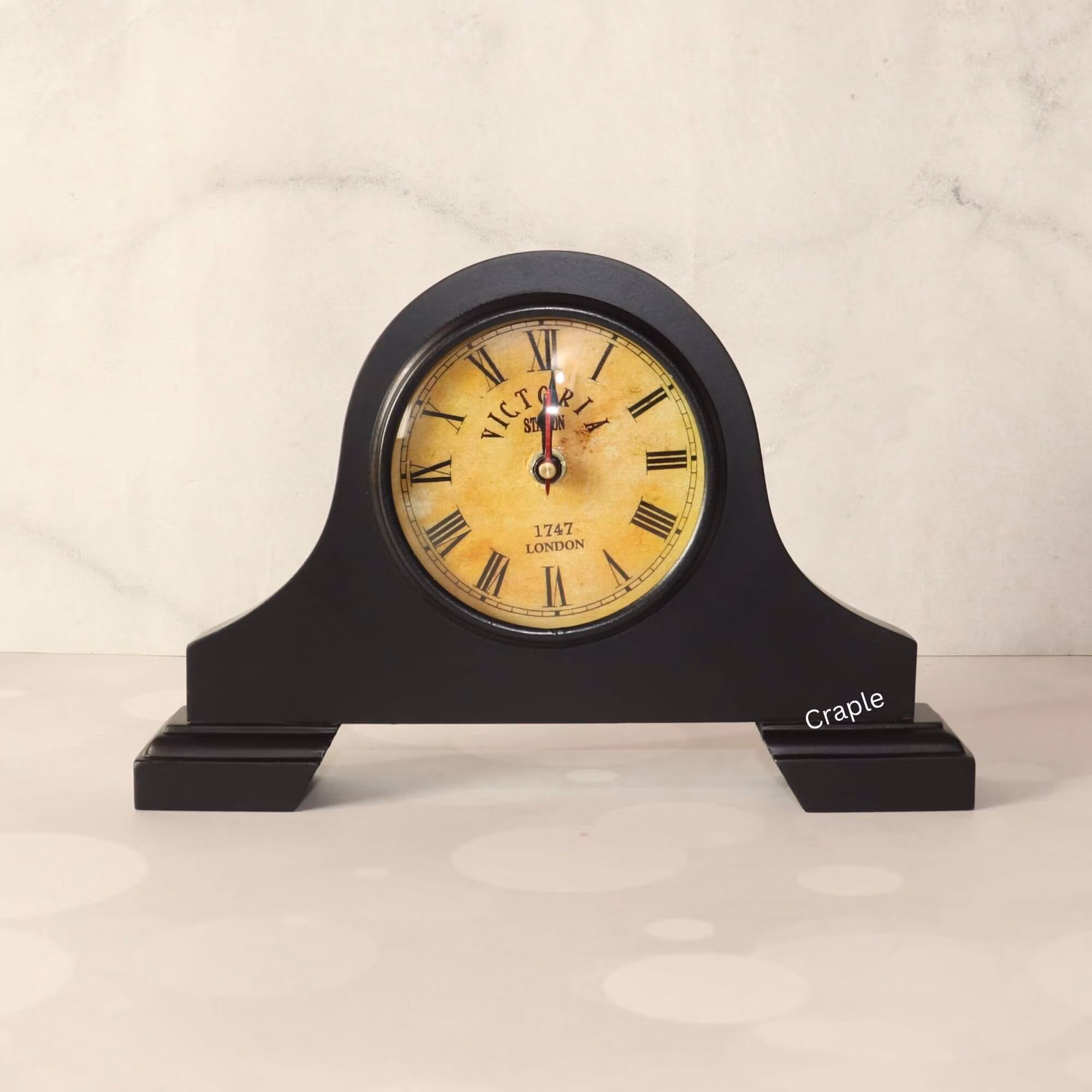 Vintage Victoria-style mantel clock with a black antique finish, a round aged-yellow dial, and classic Roman numerals.