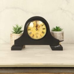 The vintage-style black mantel clock sitting on a tabletop, showing its elegant design in a home setting.