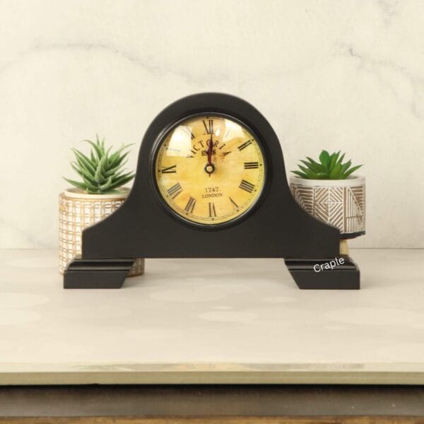 The vintage-style black mantel clock sitting on a tabletop, showing its elegant design in a home setting.