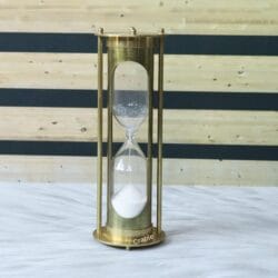 Vintage brass 5-minute hourglass with a shiny finish and pillar design, showing white sand flowing through the glass.