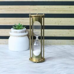 Elegant brass sand timer displayed as a decorative piece on a desk next to a small plant.