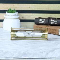 The brass 5-minute sand timer resting horizontally on a desk next to vintage leather-bound books.