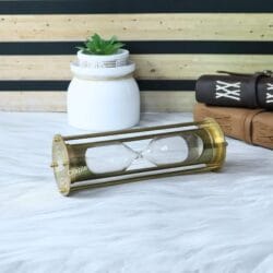 Top-down angled view of the brass hourglass lying on its side, showing the base and frame details.