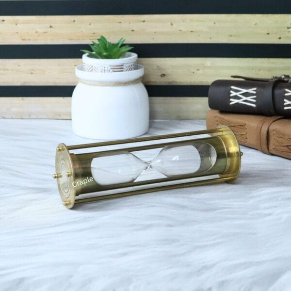 Top-down angled view of the brass hourglass lying on its side, showing the base and frame details.