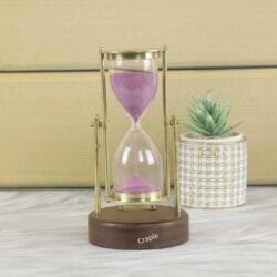 A vintage Royal Navy hourglass with pink sand, a shiny brass swivel stand, and a round wooden base.