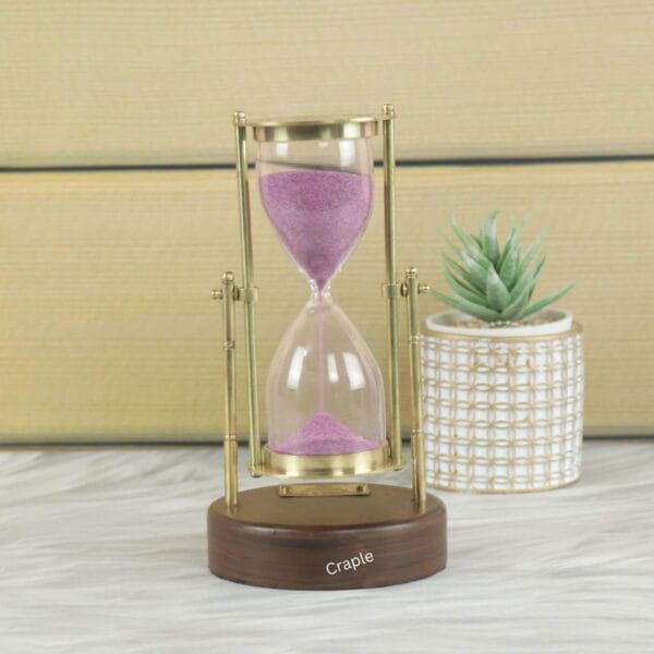 A vintage Royal Navy hourglass with pink sand, a shiny brass swivel stand, and a round wooden base.