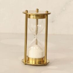 A 1-minute hourglass with a shiny brass frame and clean white sand, standing upright on a marble surface.