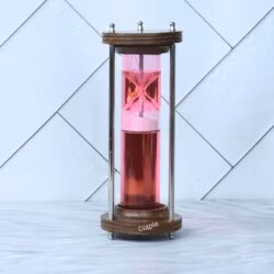 A modern liquid hourglass with a wood and brass frame, featuring a floating pink timer mechanism in red liquid.