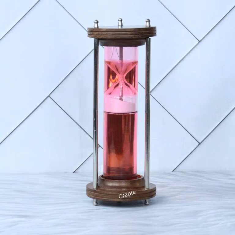 A modern liquid hourglass with a wood and brass frame, featuring a floating pink timer mechanism in red liquid.