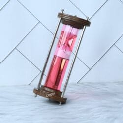 The wood and brass liquid hourglass tilted at an angle, showing the pink timer element floating within the red liquid.