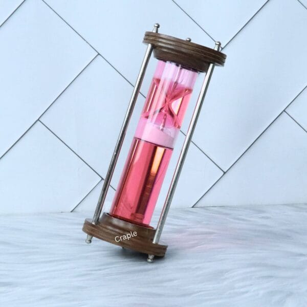 The wood and brass liquid hourglass tilted at an angle, showing the pink timer element floating within the red liquid.