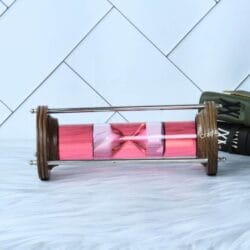 The decorative liquid sand timer lying horizontally, showcasing the wood and brass construction.