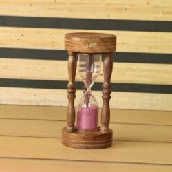 A handcrafted 5-minute hourglass with a brown wooden frame, ornate pillars, and vibrant pink sand.