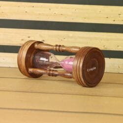 Angled view of the decorative wooden sand timer with pink sand lying on its side.